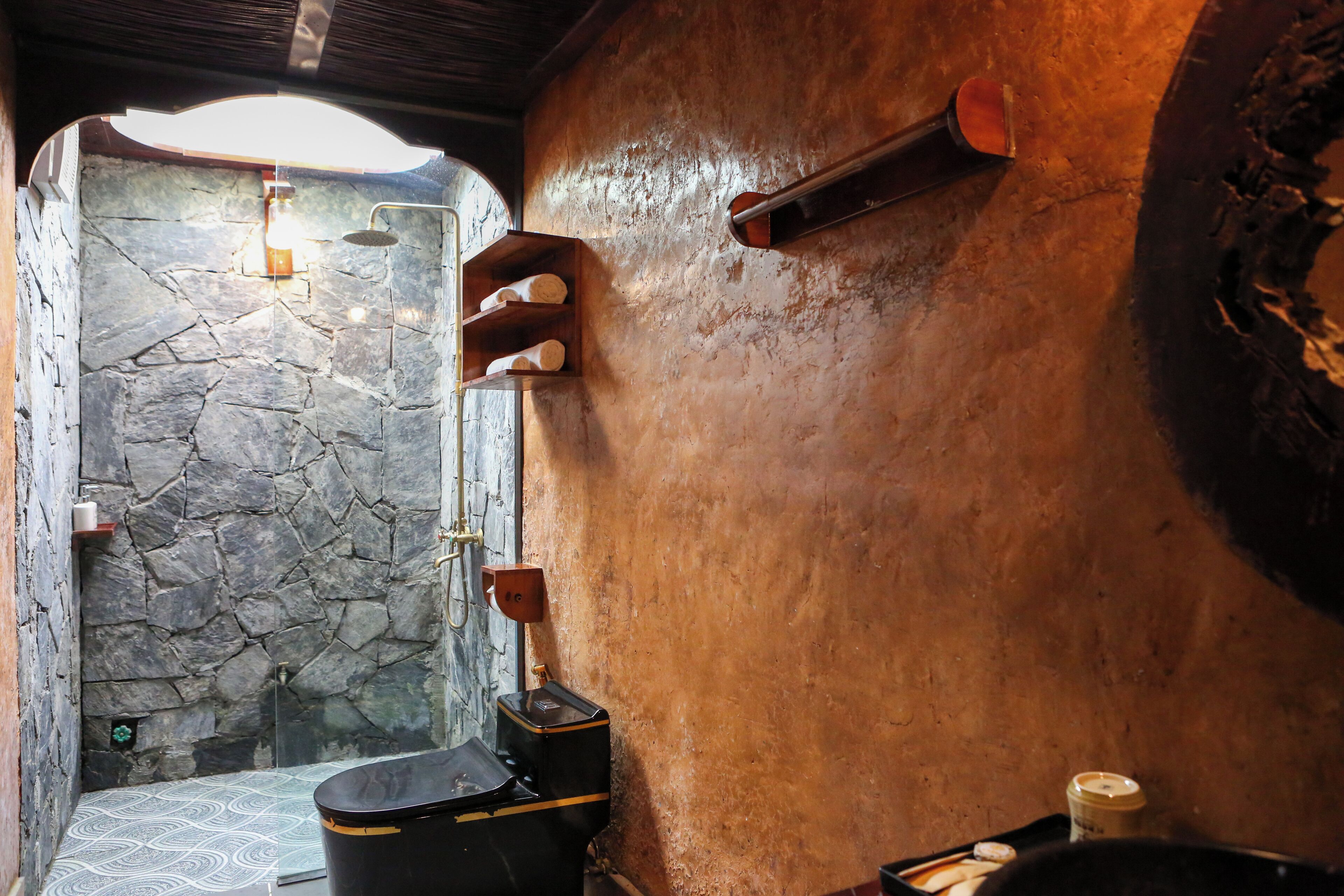A rustic bathroom with a stone shower, wooden shelves, and a vintage toilet.