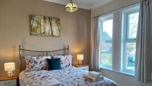 A bedroom with a bed, two bedside tables, a window with curtains, a hanging light fixture, and a painting on the wall. - Charming 4-bed Victorian House in Retford (Retford)