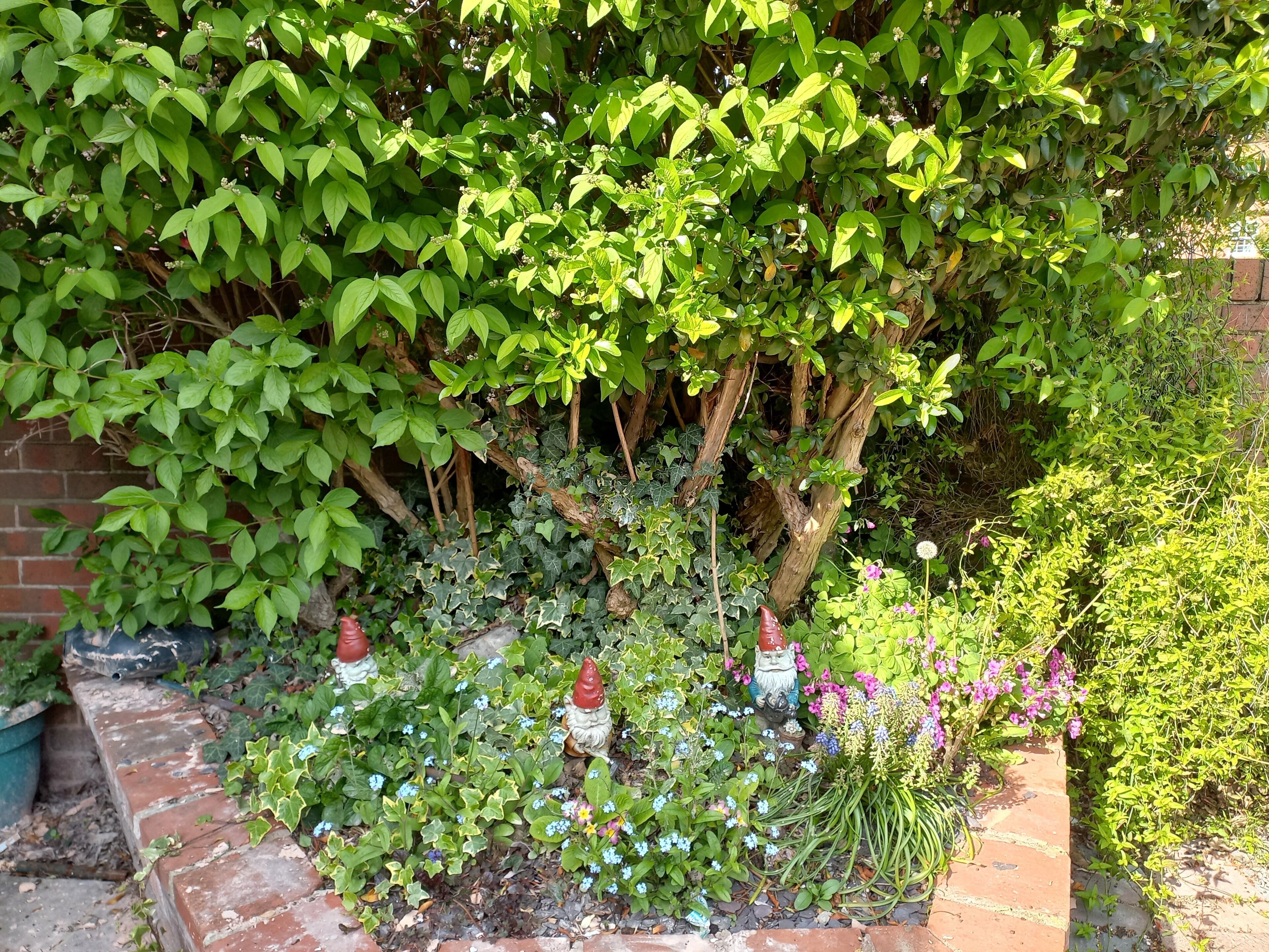 A garden with a variety of plants and flowers, a brick pathway, and decorative statues.