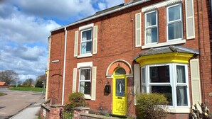 A two-story brick house with a yellow front door, white window shutters, and a small garden. - Charming 4-bed Victorian House in Retford (Retford)