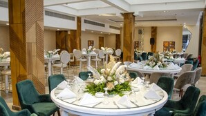 A spacious banquet hall with round tables set for dining, surrounded by green upholstered chairs. - Helnan Hotel Port Fouad (Port Fuad)