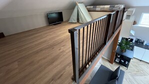 Parvelle sijoitettu makuuhuone, jossa on puulattia, sänky, televisio, teltta ja keittiöalue, jossa on myös kasvi.