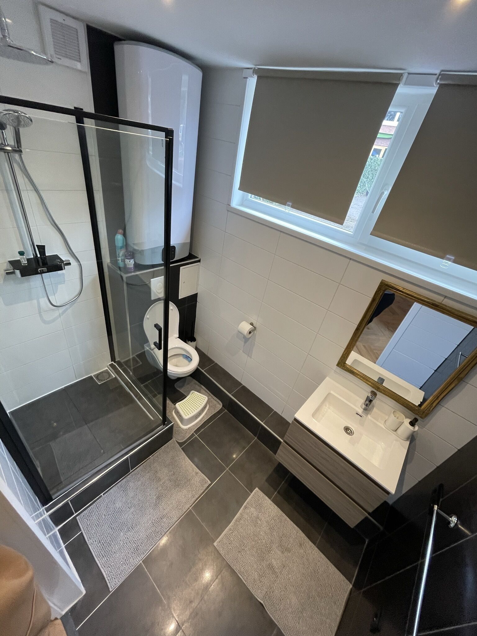 A modern bathroom with a glass-enclosed shower, a toilet, a sink with a mirror, and a window above the sink.
