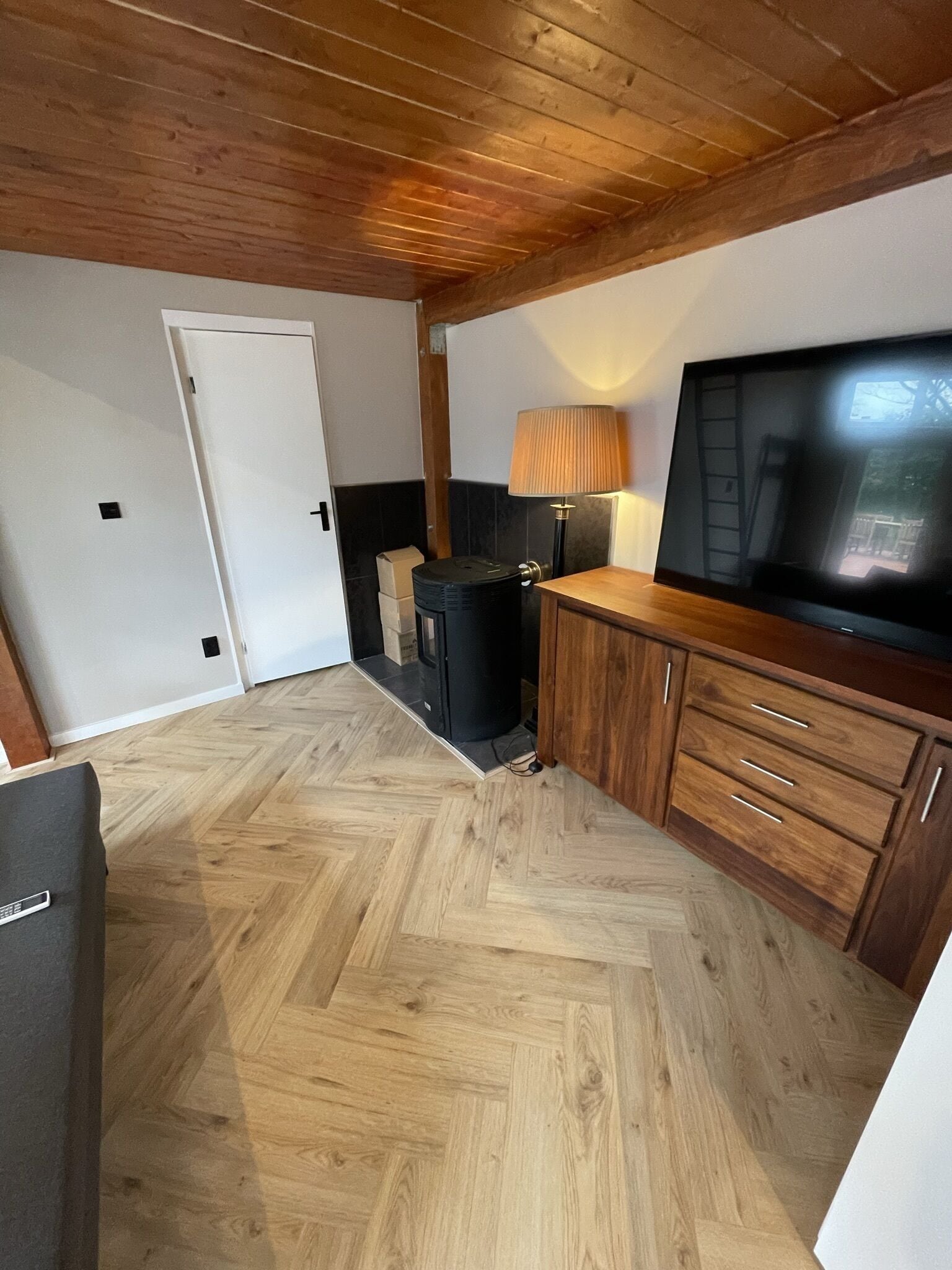 Een compacte woonruimte met een houten plafond, een televisie, een lamp en een visgraatvloer.