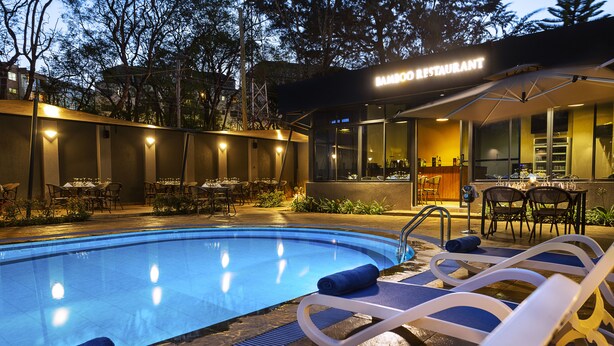 A poolside area with lounge chairs and a restaurant named "Bamboo Restaurant" in the background. - Saggys Suites Hotel & Spa (Nairobi)