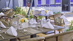 An outdoor dining area with tables set for two, featuring wicker chairs, clear glassware, and white napkins. - Saggys Suites Hotel & Spa (Nairobi)