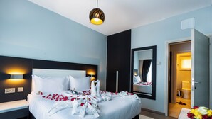 A modern hotel room with a large bed, bedside tables, a mirror, and a bathroom visible through an open door. - Saggys Suites Hotel & Spa (Nairobi)