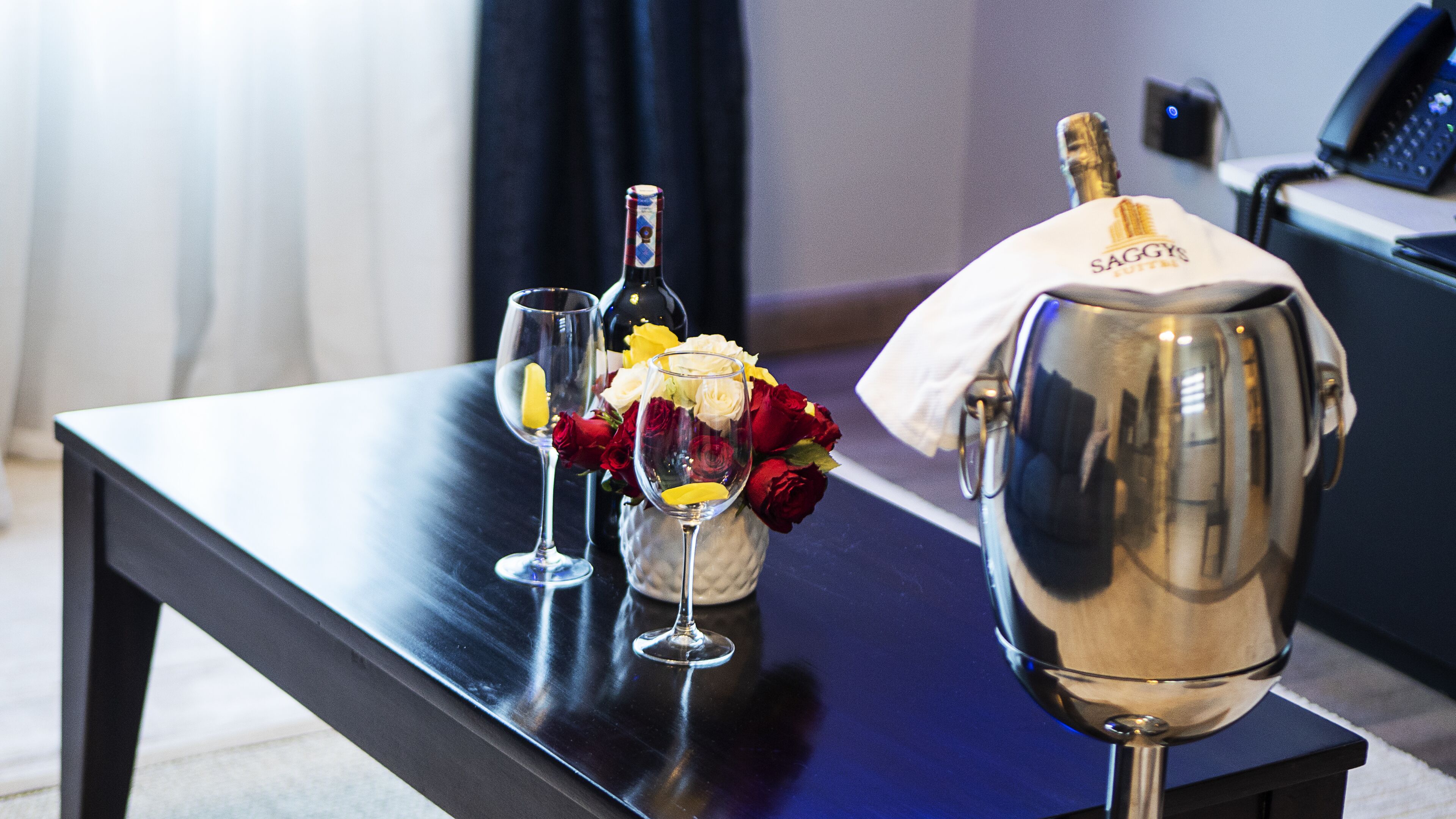 A table with a champagne bottle, two wine glasses, and a vase with roses.