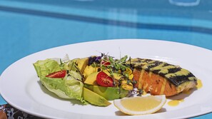 A plate with grilled salmon, avocado, and a salad with tomatoes and greens.