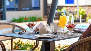 A table set for breakfast with a glass of orange juice, a dessert in a glass bowl, and a white ceramic jug.