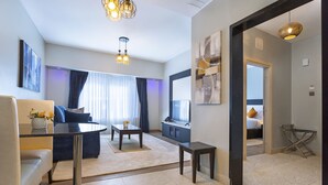 A modern living room with a sofa, coffee table, and a dining table. There is a view of a bedroom through an open door. - Saggys Suites Hotel & Spa (Nairobi)