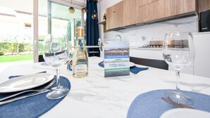 Una mesa de comedor servida con platos, cubiertos y copas de vino, una botella de CaMaïol, y un folleto de MyGardaHoliday Homes.