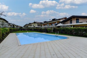 A swimming pool surrounded by a paved deck, with a row of houses in the background.