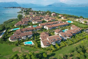 Eine Vogelperspektive auf eine Küstenwohngegend mit mehreren Häusern, von denen einige Swimmingpools haben, vor dem Hintergrund eines großen Gewässers und Bergen.