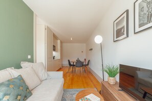 A modern living room with a sofa, a coffee table, a TV, and a dining area with chairs and a table. - LEGACY OPORTO PREMIUM APARTMENT C by VACATIONY (Oporto)