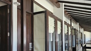 Un pasillo con puertas de madera y suelo de baldosas, que conduce a habitaciones con ventanas de vidrio.