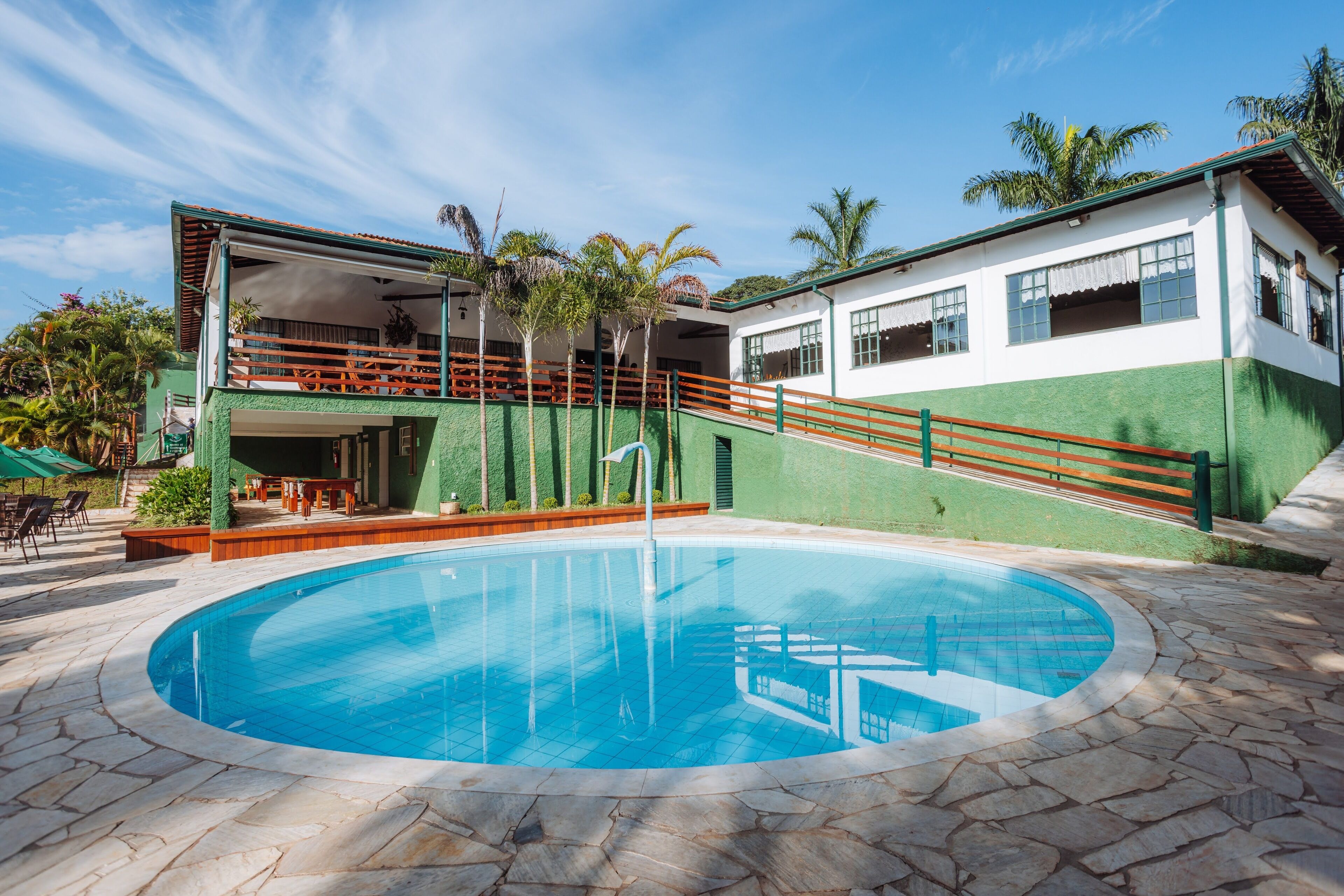 A swimming pool with a stone border, a wooden deck, and a building with a green and white facade.