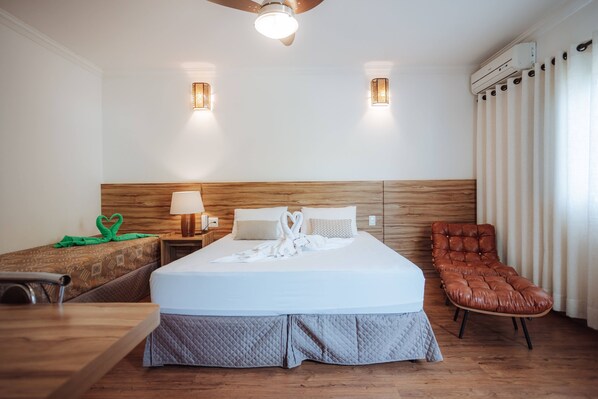 Een hotelkamer met een bed, een houten hoofdbord, een bureau, een stoel en een plafondventilator.