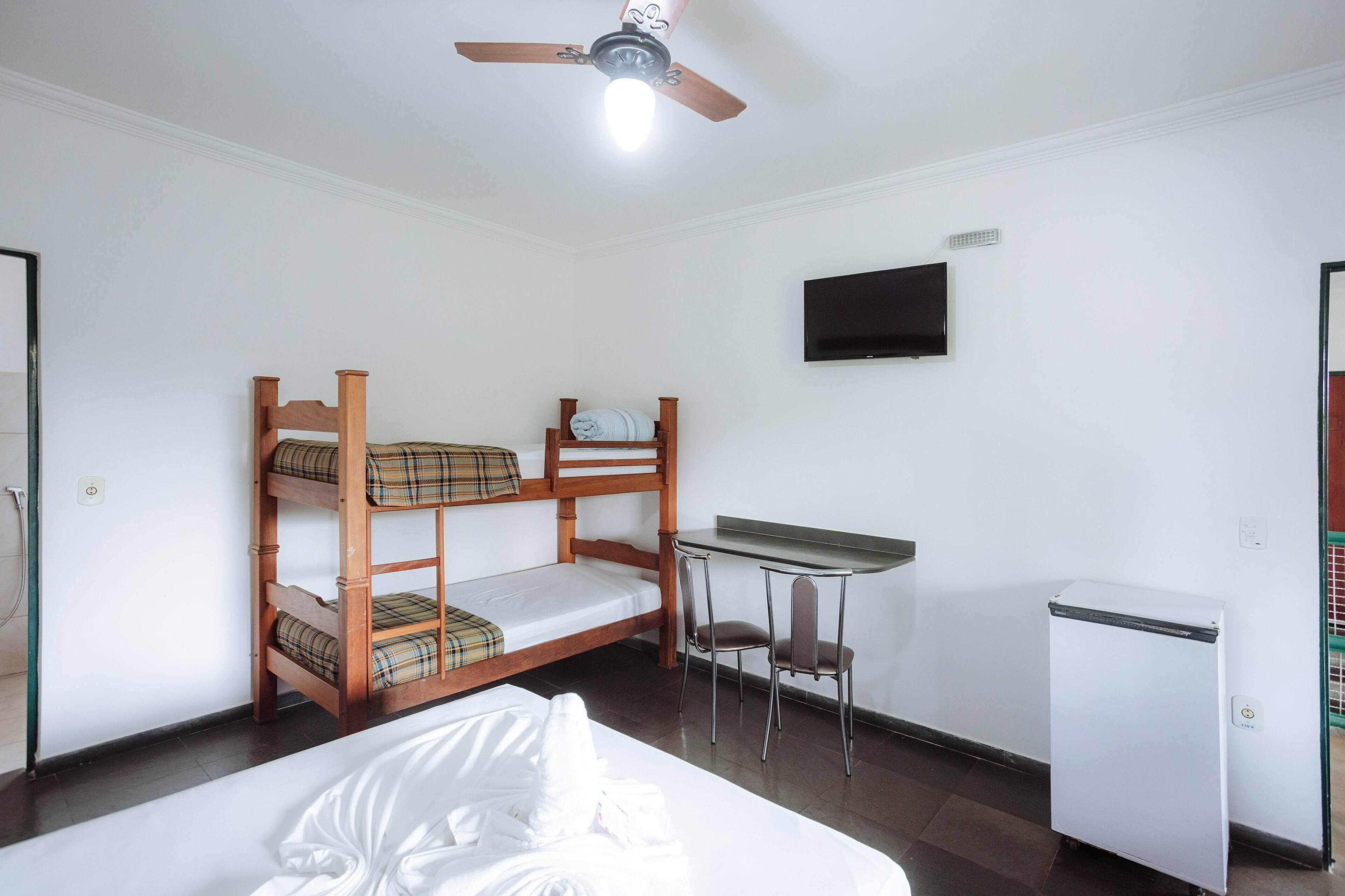 Quarto com beliche, escrivaninha, cadeira e um pequeno frigorífico.