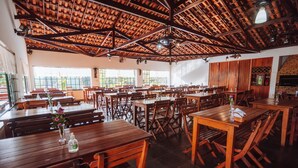 A spacious restaurant with wooden tables and benches, large windows, and a high wooden ceiling. - Hotel Fazenda Vale Amanhecer  (Igarape)