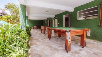 Espaço com mesa de bilhar, paredes verdes e chão de pedra, rodeado por plantas.