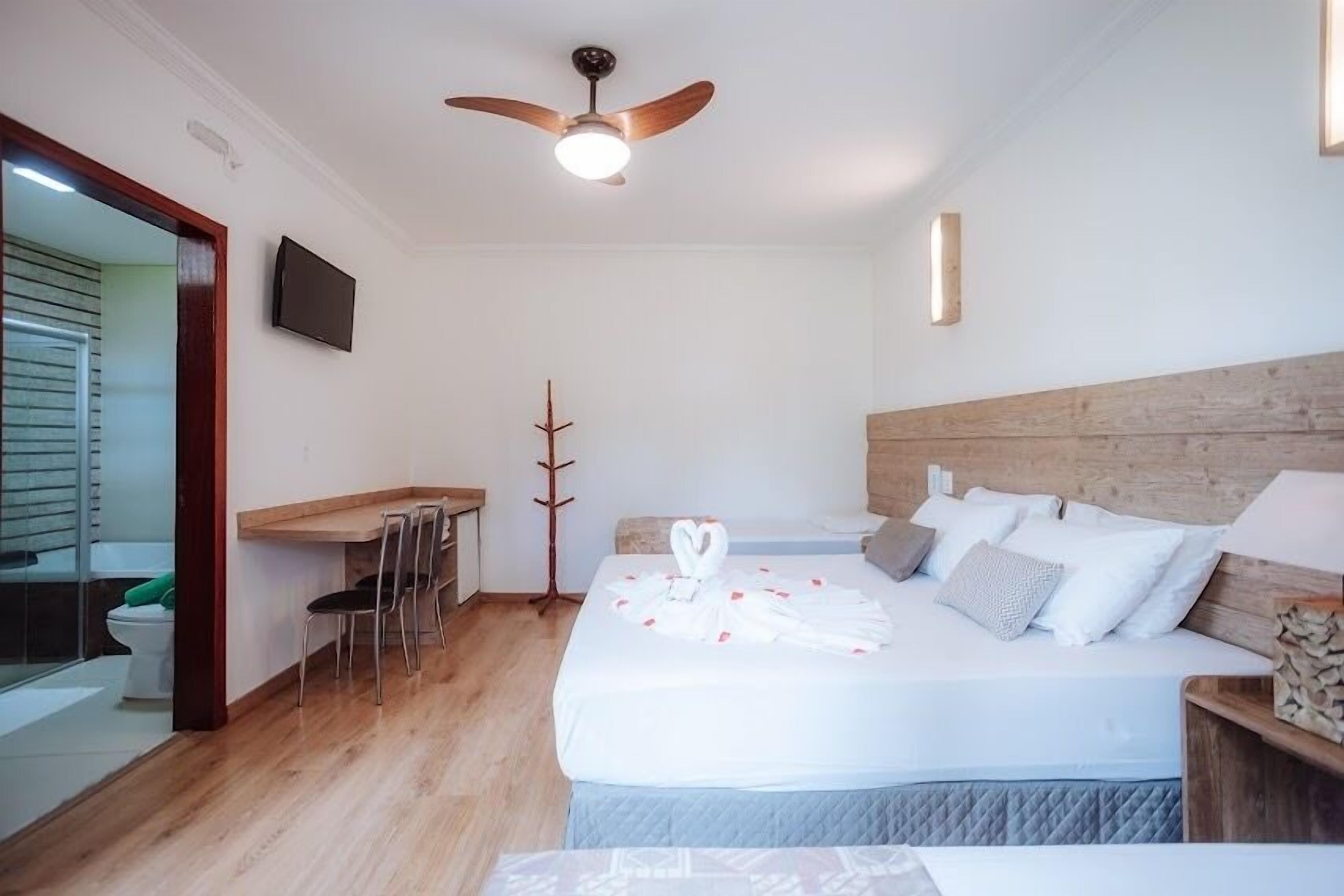 A hotel room with a bed, a desk, a chair, a TV, and a ceiling fan.
