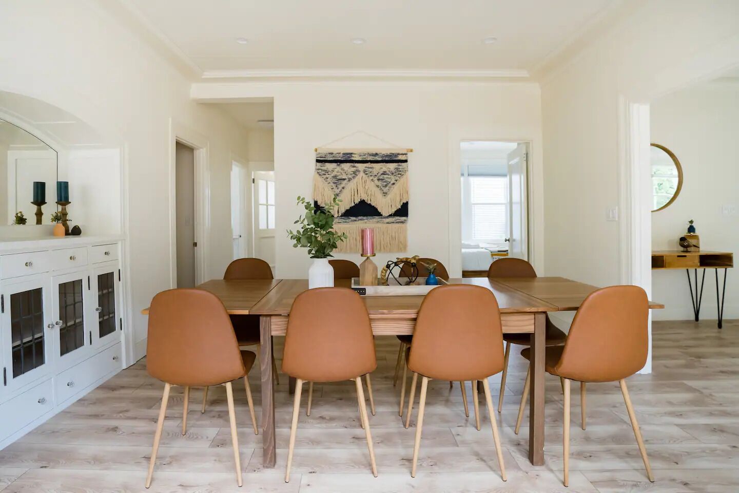 Un comedor con una mesa de madera, seis sillas marrones y un aparador blanco con puertas de cristal.