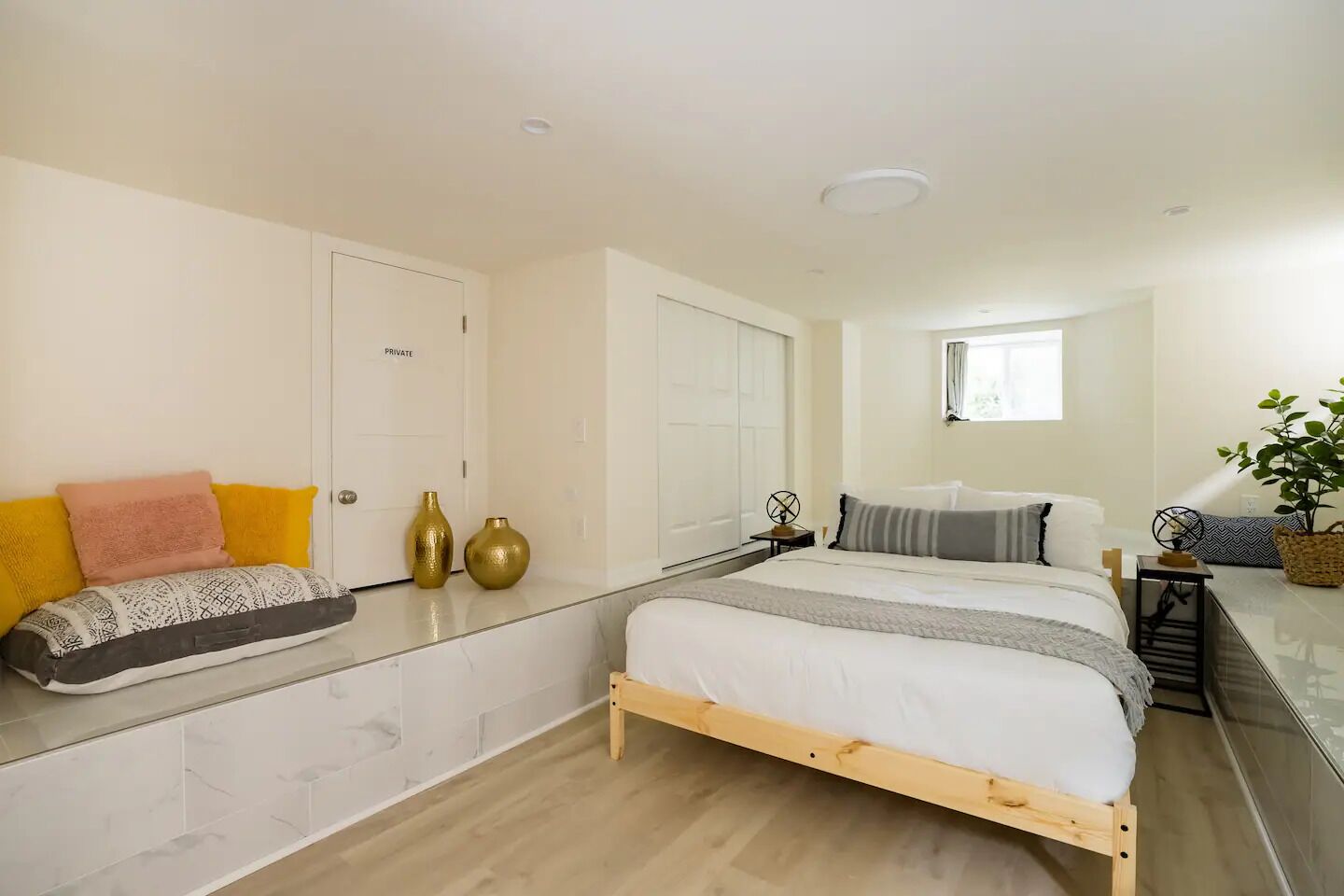 A bedroom with a bed, bedside tables, a window, and a plant.