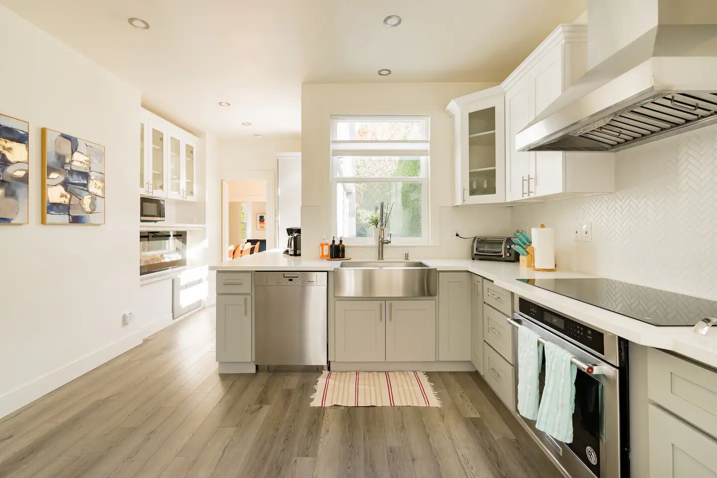 A modern kitchen with white cabinetry, stainless steel appliances, and a large window providing natural light.
