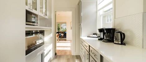 Une cuisine moderne avec des meubles blancs, un four encastré et un espace dédié à la préparation du café.