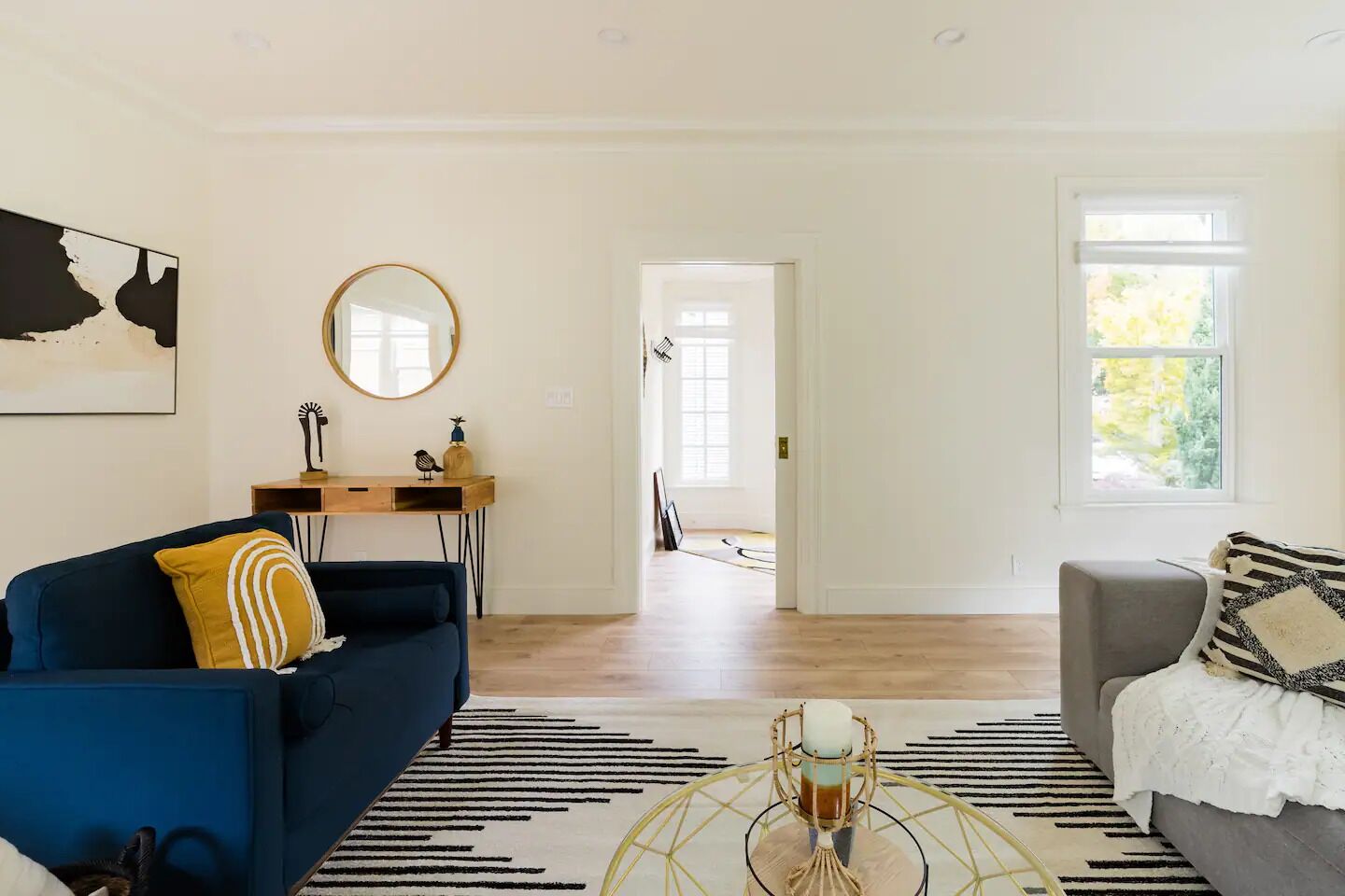A spacious living room with a blue sofa, a grey armchair, a coffee table, and a large window.