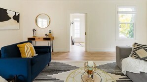 Amplia sala de estar con un sofá azul, un sillón gris, una mesita de centro y un ventanal grande.