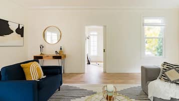 A spacious living room with a blue sofa, a grey armchair, a coffee table, and a large window.
