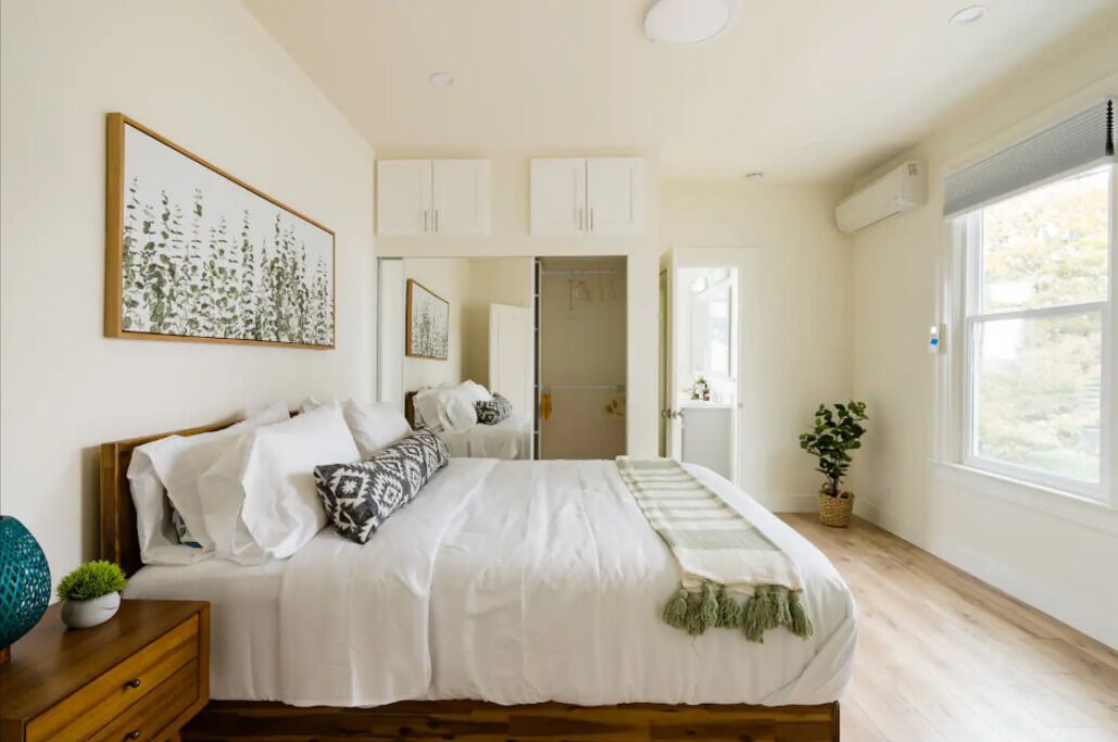 A bedroom with a bed, a bedside table, a nightstand, a window, and a door leading to a bathroom.