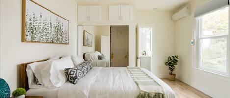 A bedroom with a bed, a bedside table, a nightstand, a window, and a door leading to a bathroom.