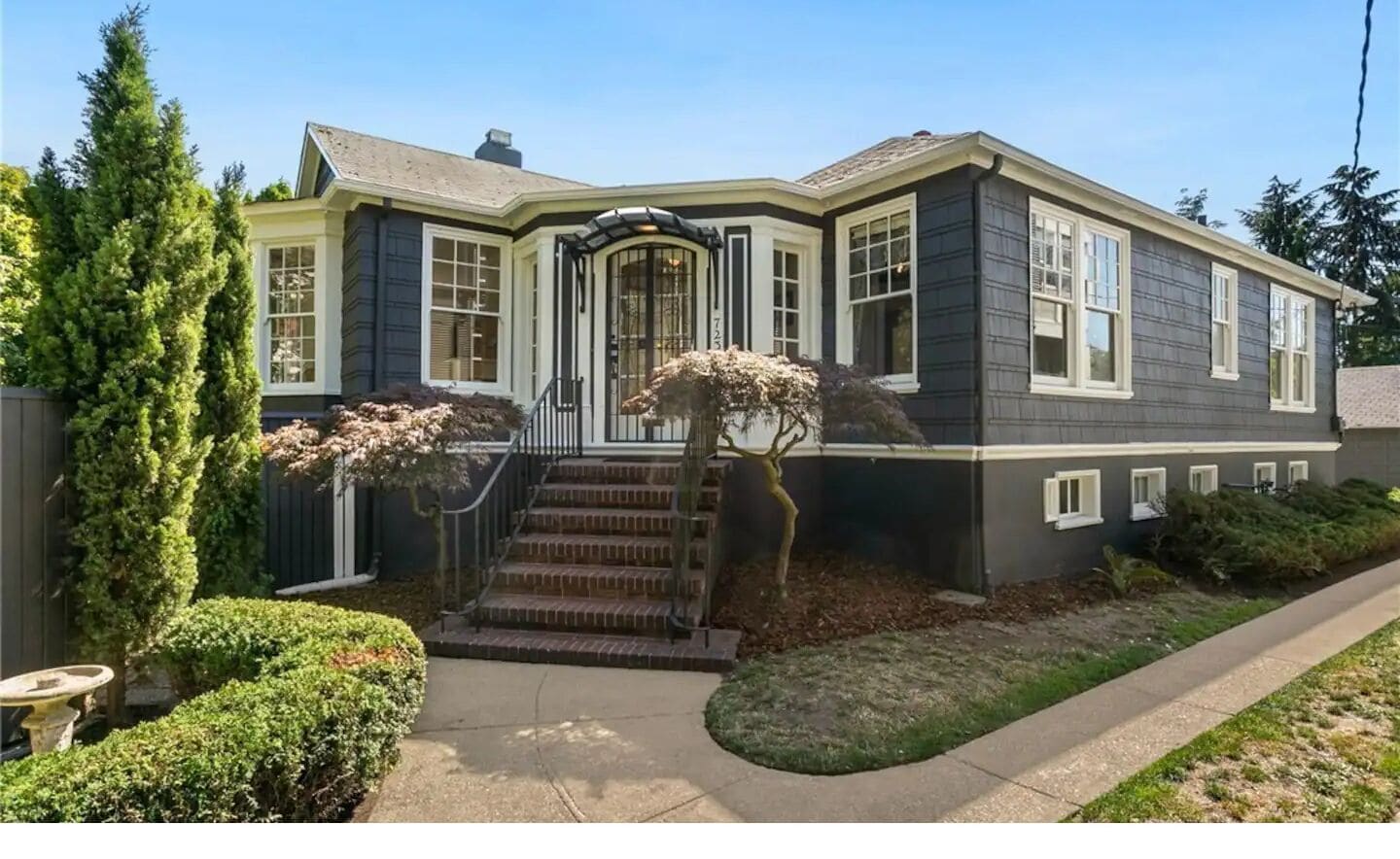 A two-story house with a front entrance, a covered porch, and a small front yard with a tree and shrubs.