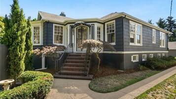 A two-story house with a front entrance, a covered porch, and a small front yard with a tree and shrubs.