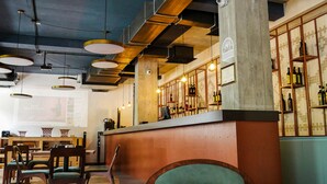 A restaurant interior with exposed ceilings, hanging pendant lights, wooden tables, and chairs. - Paliani Hotel (Mestia)