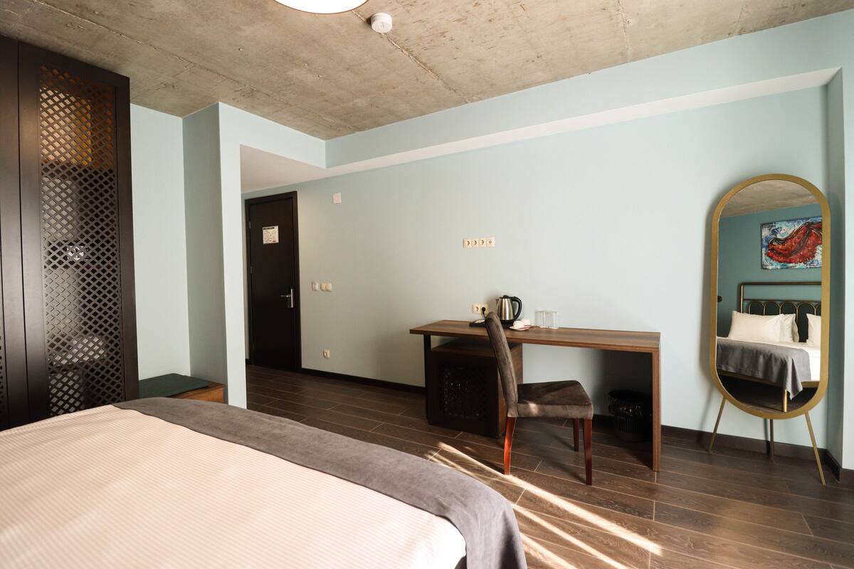 Ein Hotelzimmer mit Bett, Schreibtisch, Stuhl, Spiegel und Tür.