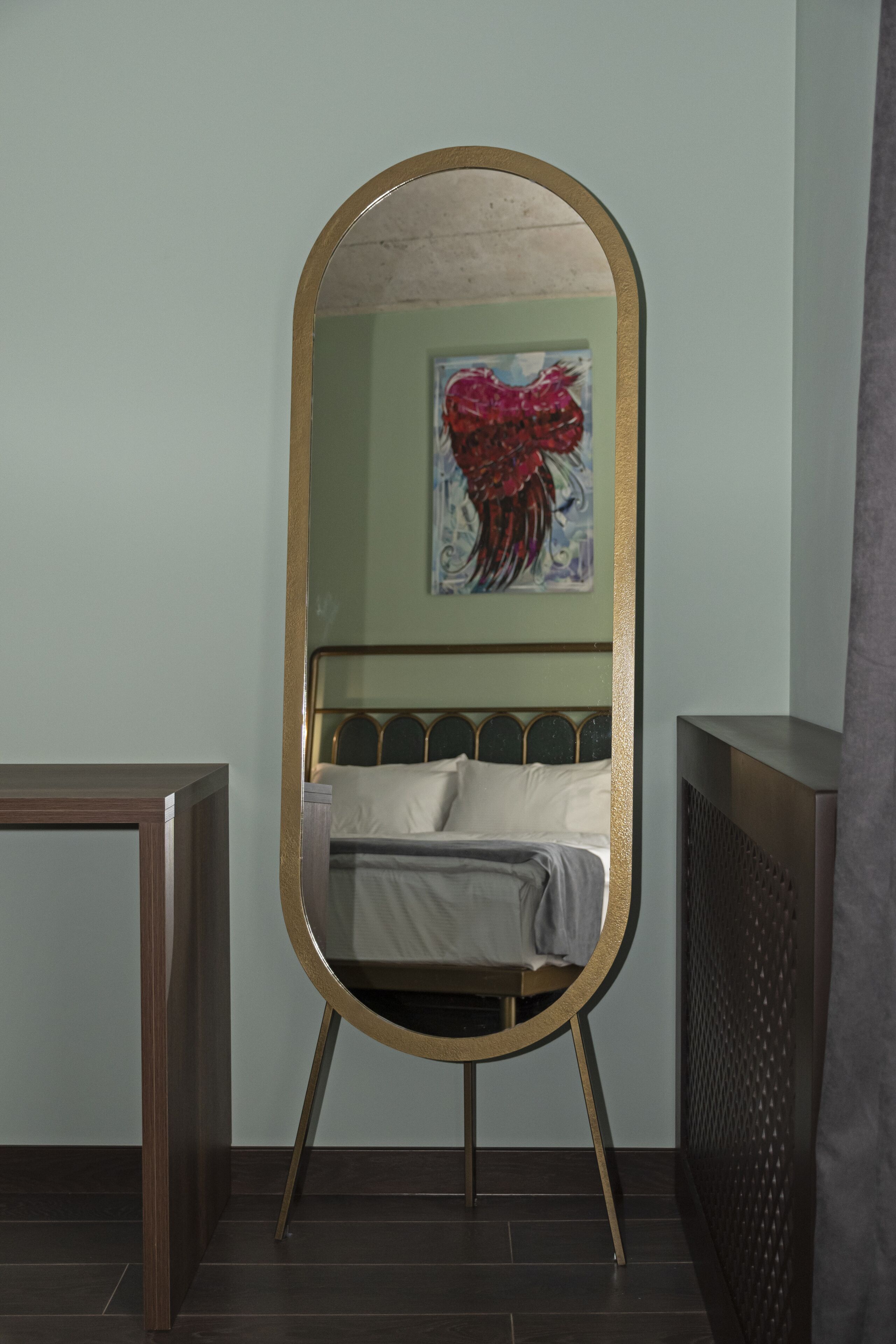 A room with a bed, a round mirror with a gold frame, and a painting on the wall.