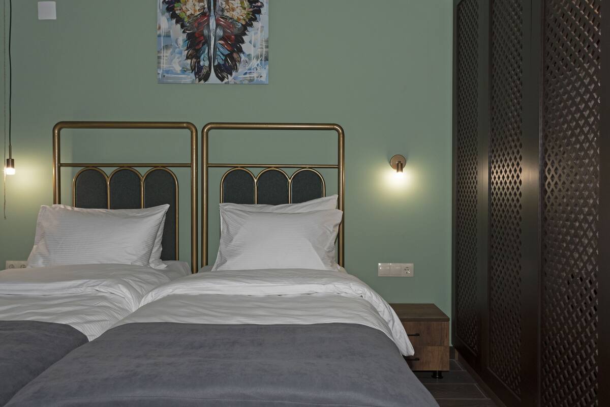 Ein Doppelbett mit Metallgestell, zwei Nachttische, eine Wandleuchte und ein dekoratives Gemälde.
