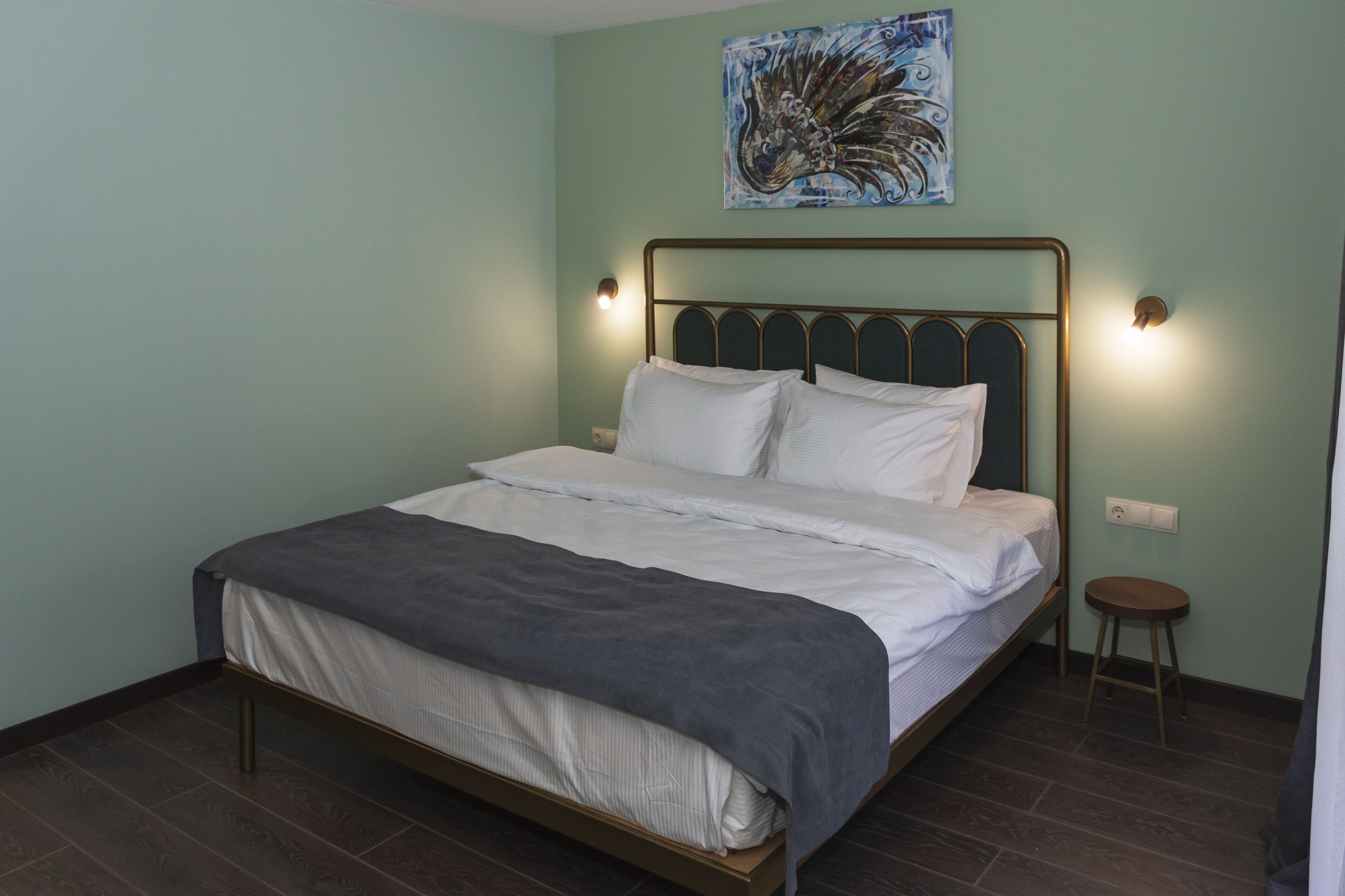 A neatly made bed with a grey blanket, a metal headboard, and two wall-mounted lights.