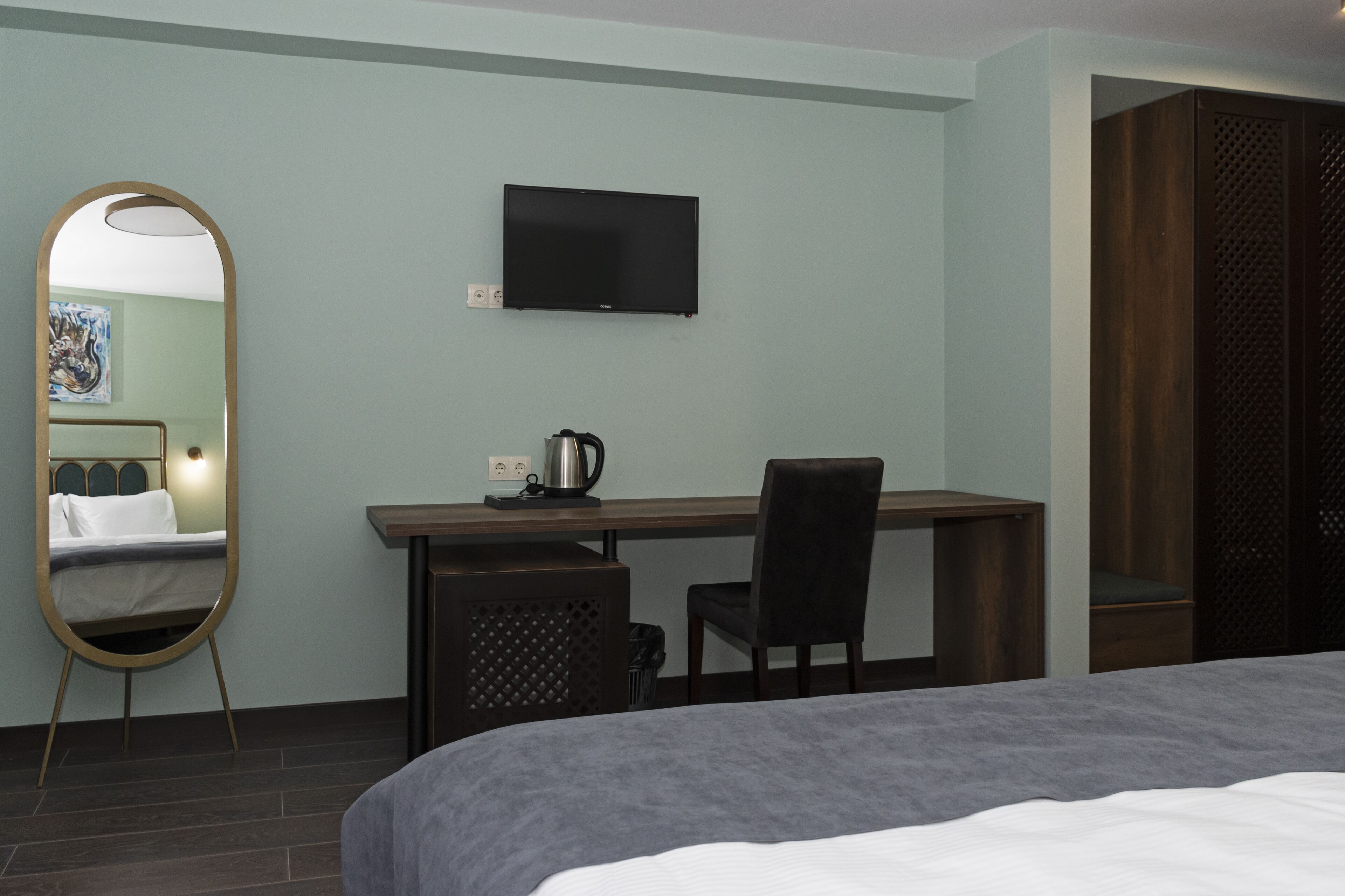 Une chambre d’hôtel comprenant un lit, un bureau avec une chaise, un téléviseur fixé au mur et un grand miroir.