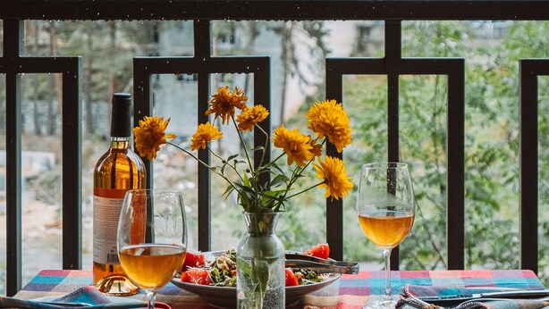 A table set with food and drinks, a bottle, and a glass of wine, with a view of buildings and trees in the background. - Paliani Hotel (Mestia)
