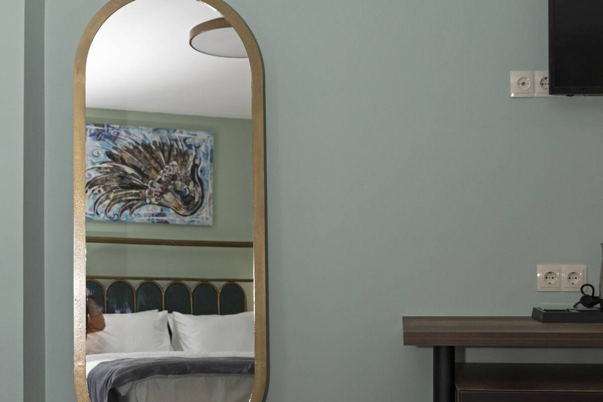 Ein Hotelzimmer mit einem Bett, einem auf einem Sockel stehenden runden Spiegel, einem Gemälde an der Wand und einem Fernseher.