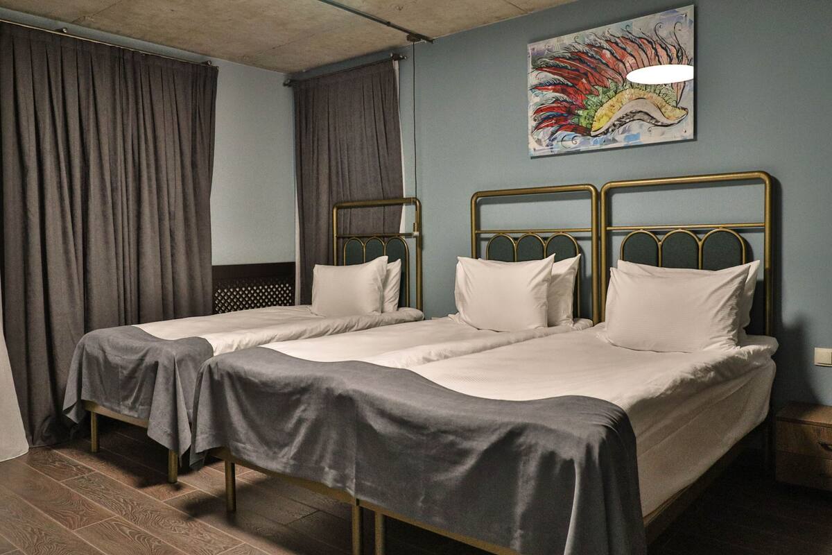 Ein Zimmer mit zwei Einzelbetten, Holzboden, einem Gemälde an der Wand und einem Nachttisch mit Lampe.