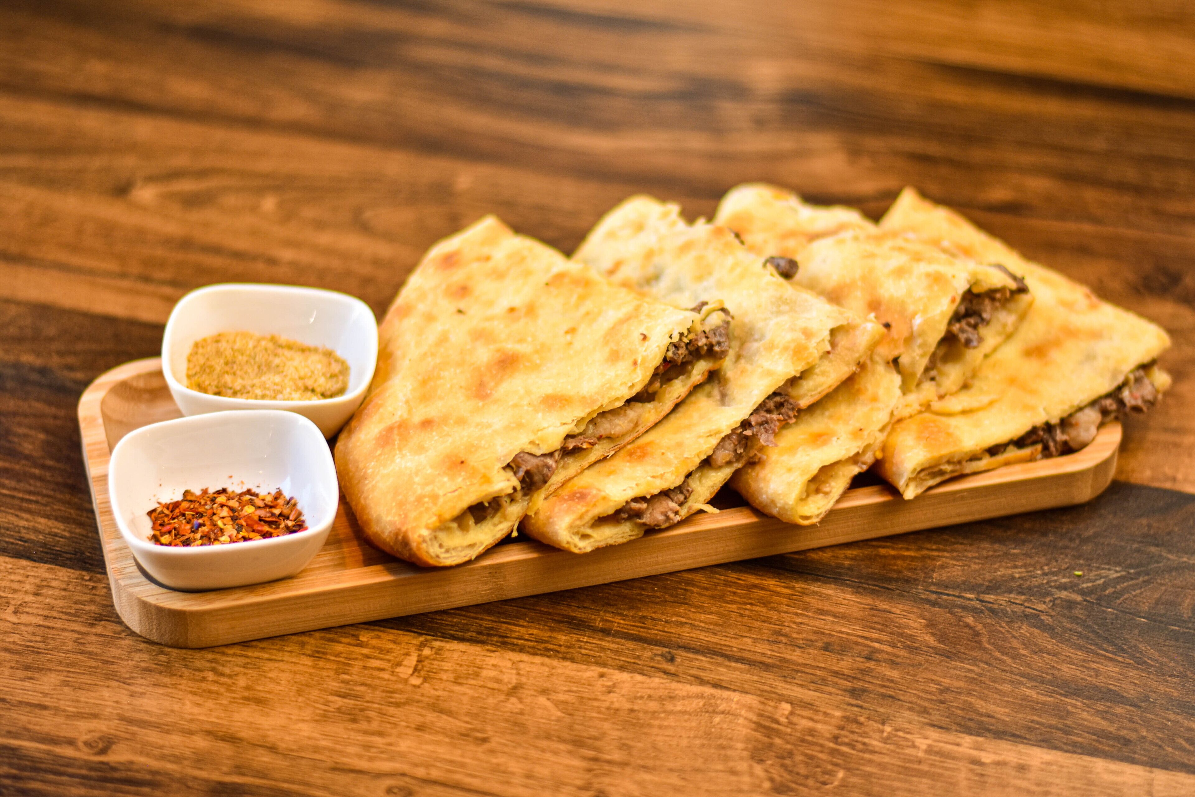 Une planche en bois servant de plat, sur laquelle on trouve plusieurs quesadillas pliées et deux petits bols d’assaisonnement.