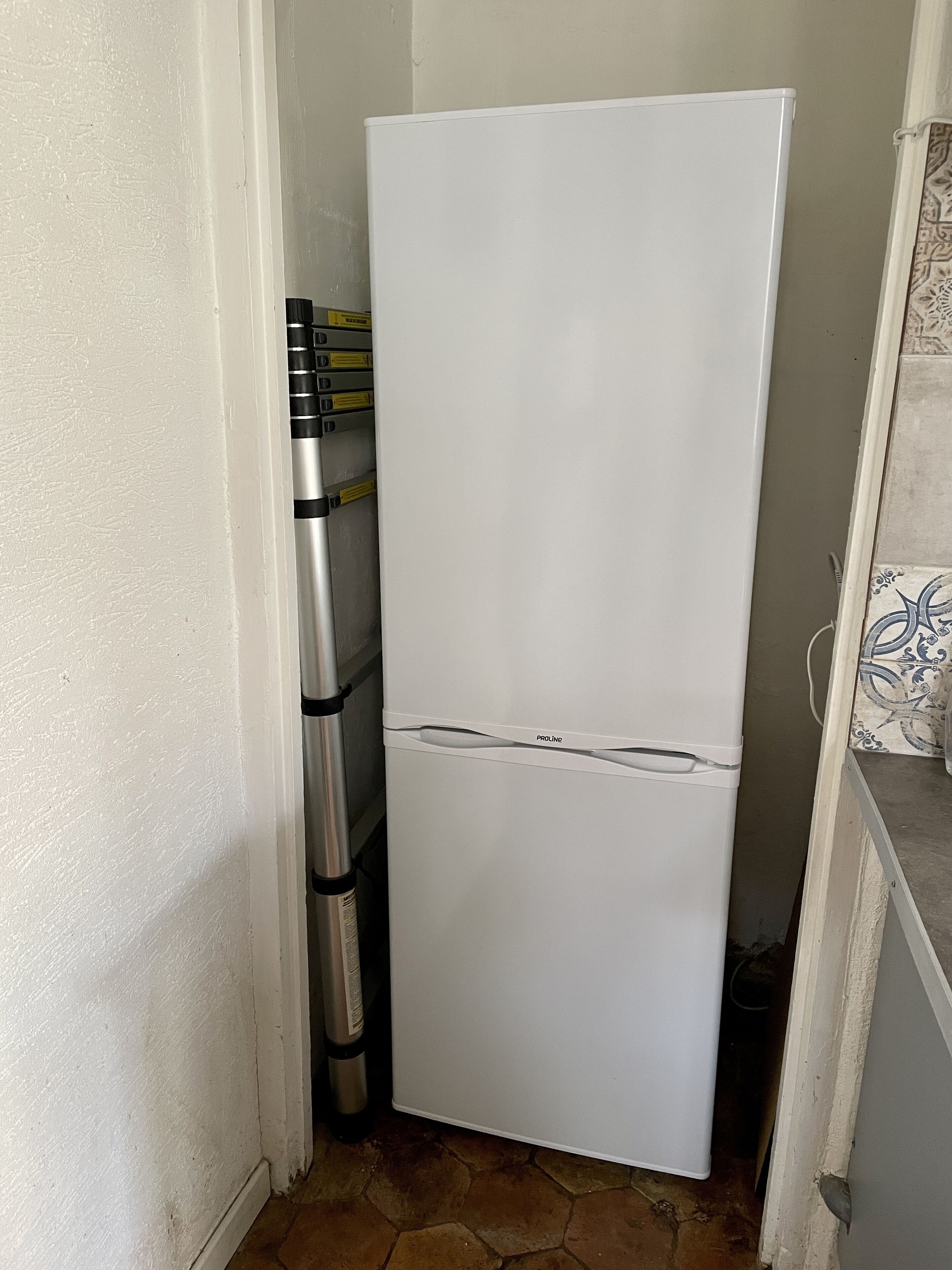 A white refrigerator in a narrow kitchen space with a tiled floor.