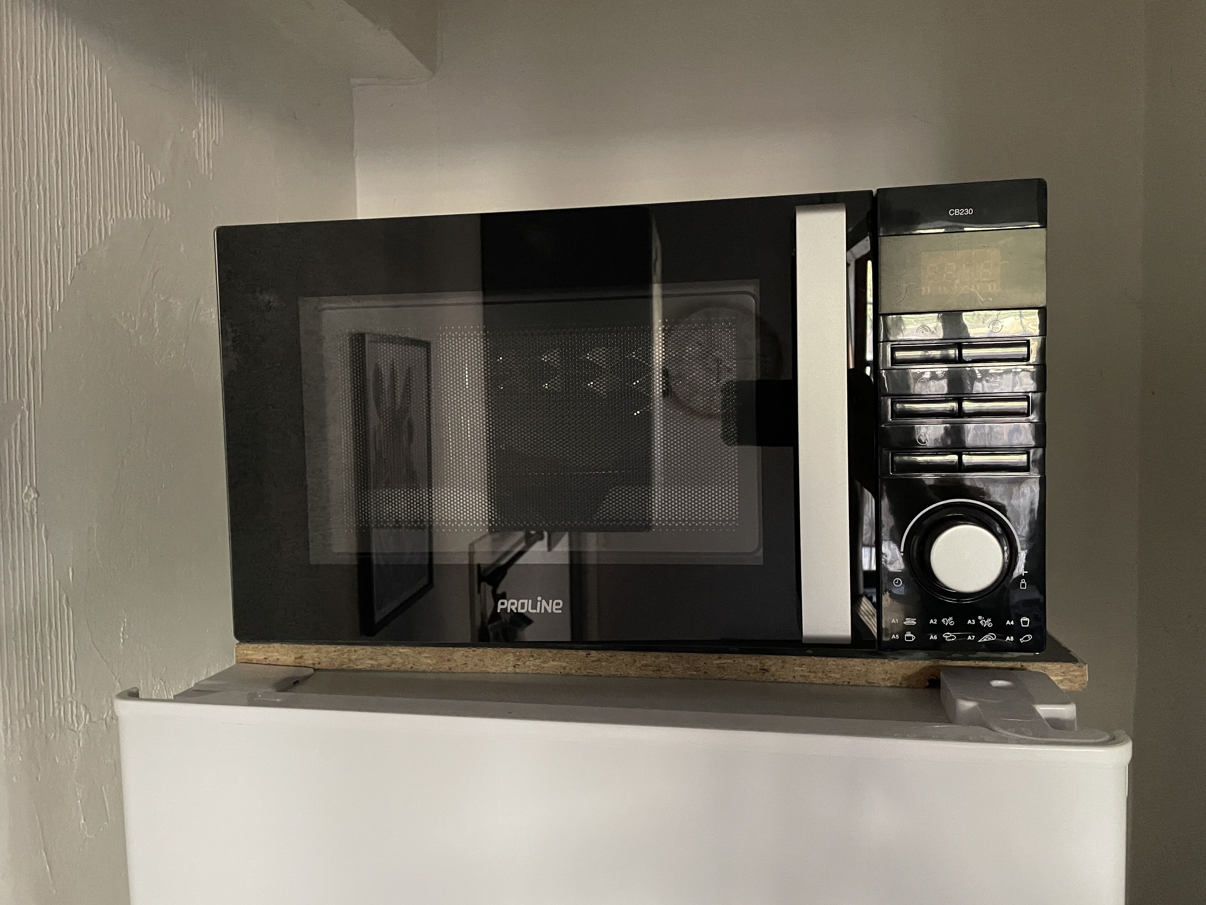Un horno microondas con pantalla digital y panel de control, sobre una superficie blanca.
