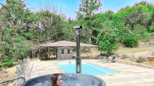 Een hottub met een houten buitenkant, een zwembad en een terras met tuinmeubilair.